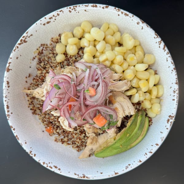 Chicken and quinoa bowl with red onion, corn, and avocado in a rustic white bowl.