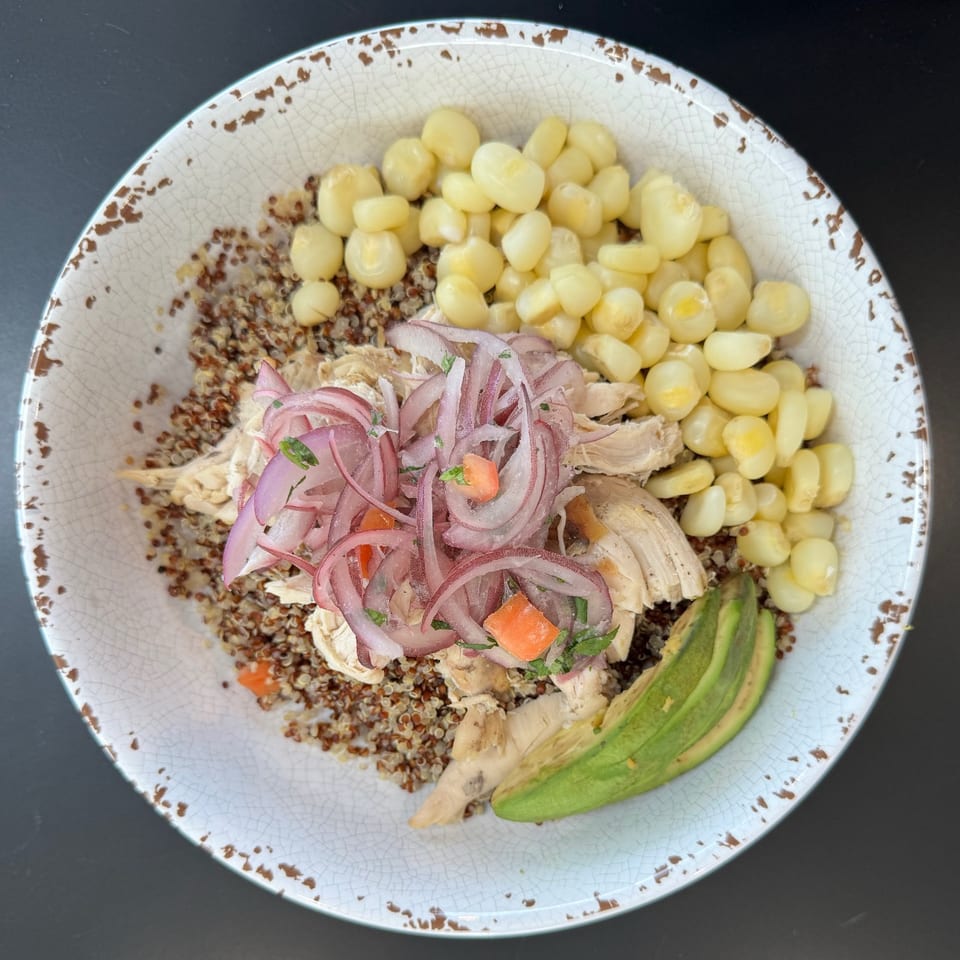 Chicken and quinoa bowl with red onion, corn, and avocado in a rustic white bowl.