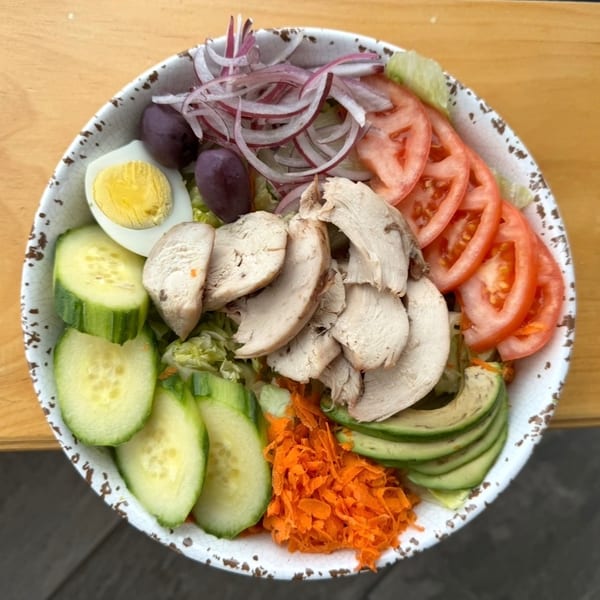 A vibrant salad bowl with chicken, cucumber, tomato, avocado, egg, olives, and red onion.