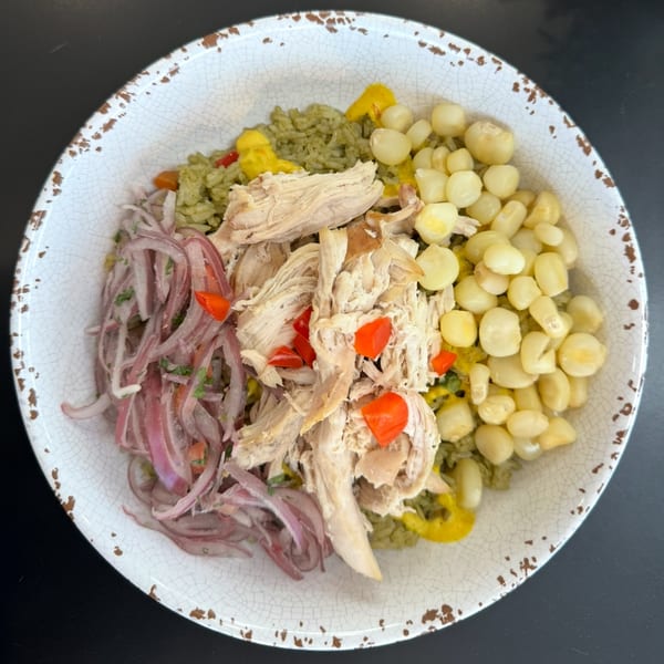 Peruvian Arroz con Pollo with shredded chicken, red onions, corn, and green rice in a white bowl.