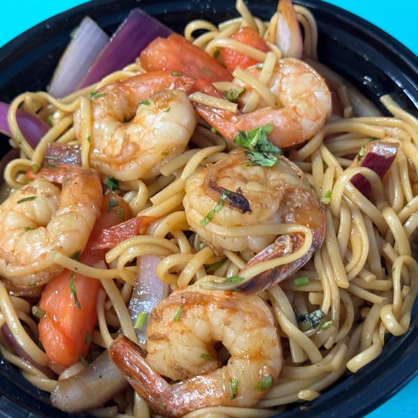 Close-up of shrimp lo mein with red onions and tomatoes in a black bowl.