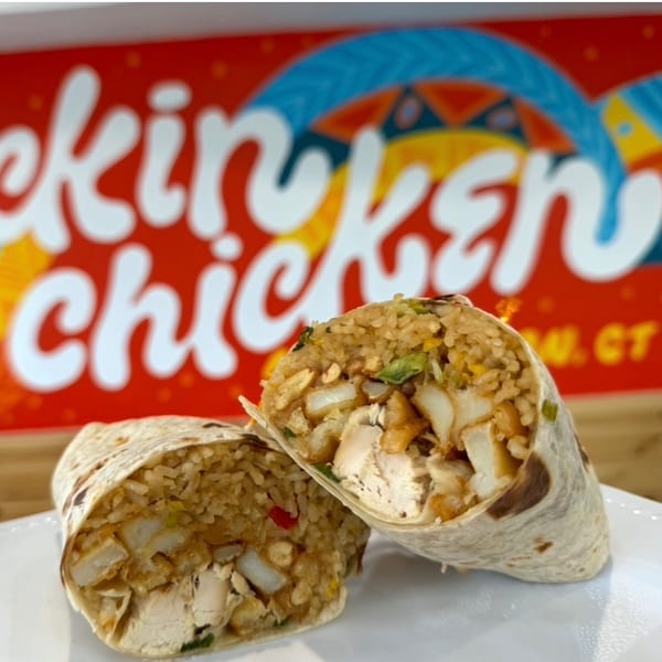 Two halves of a chicken and rice burrito on a white plate, with a colorful "Chicken" sign in the background.