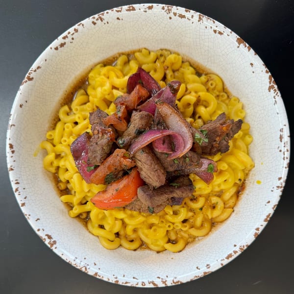 Macaroni and cheese topped with steak, red onions, and tomatoes in a rustic bowl.