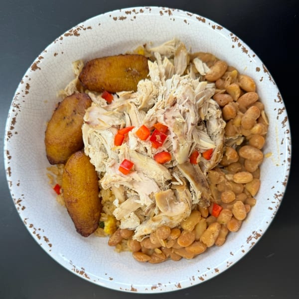 A bowl of shredded chicken, pinto beans, fried plantains, and rice with red peppers.